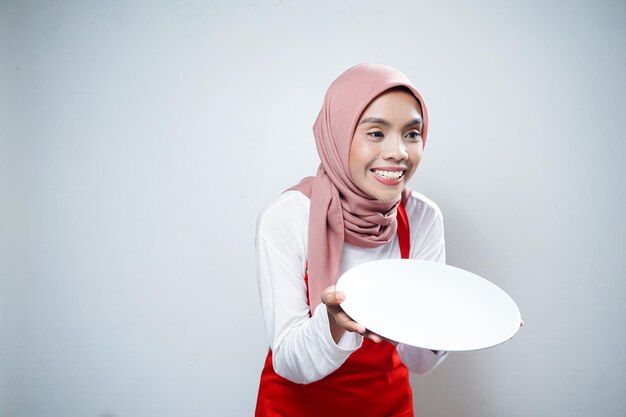 Vrolijke Aziatische moslimvrouw in rode schort met leeg bord Voedsel Advertentie Kokend concept