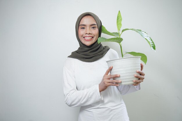 Vrolijke Aziatische moslimvrouw in t-shirt en hijab plant geïsoleerd op een witte achtergrond