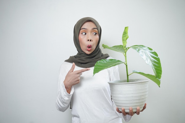 Vrolijke Aziatische moslimvrouw in t-shirt en hijab plant geïsoleerd op een witte achtergrond