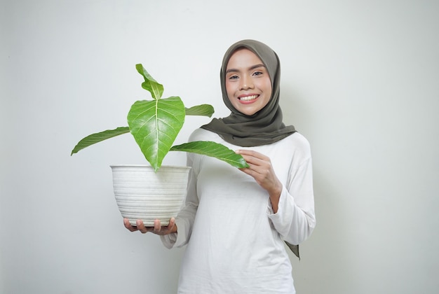 Vrolijke Aziatische moslimvrouw in t-shirt en hijab plant geïsoleerd op een witte achtergrond