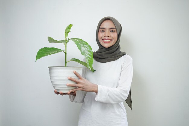 Vrolijke Aziatische moslimvrouw in t-shirt en hijab plant geïsoleerd op een witte achtergrond