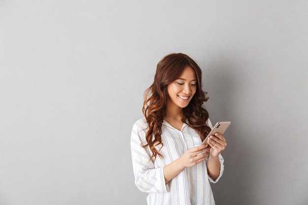 Vrolijke Aziatische vrouw geïsoleerd, met mobiele telefoon, vieren