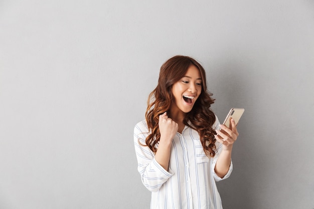 Vrolijke Aziatische vrouw geïsoleerd, met mobiele telefoon, vieren