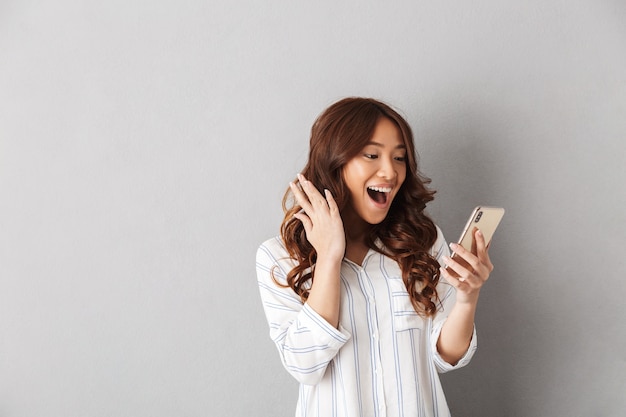 Vrolijke aziatische vrouw geïsoleerd, met mobiele telefoon, vieren