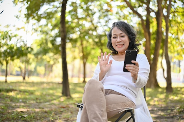 Vrolijke Aziatische vrouw uit de jaren 60 die een videogesprek voert met haar kleinkind in het park