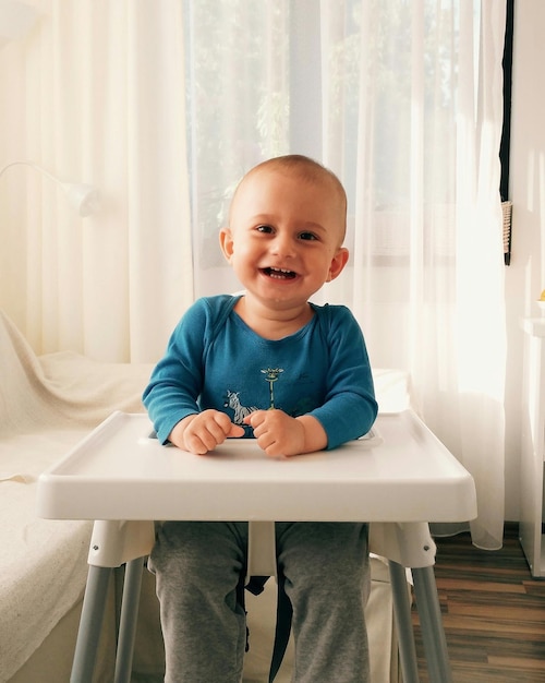 Vrolijke baby die thuis op een hoge stoel zit