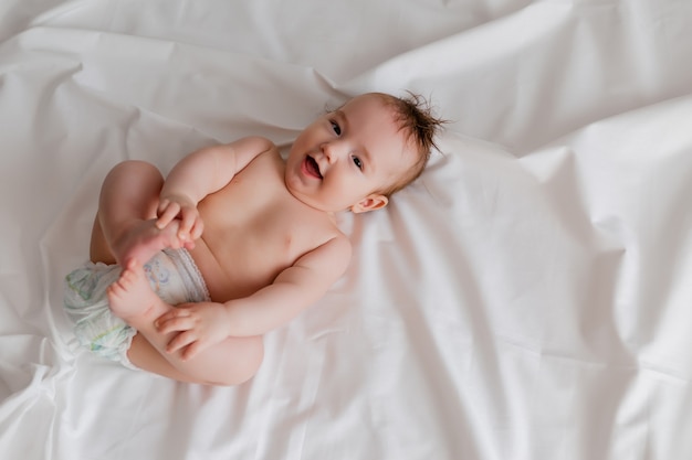 vrolijke baby in een luier ligt op zijn rug in bed op een bovenaanzicht van een wit laken