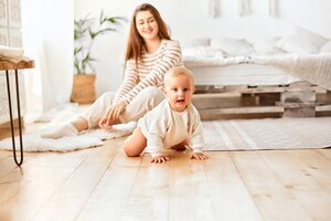 Vrolijke baby kruipt op de grond en lacht om de camera moeder op de achtergrond ouderschap