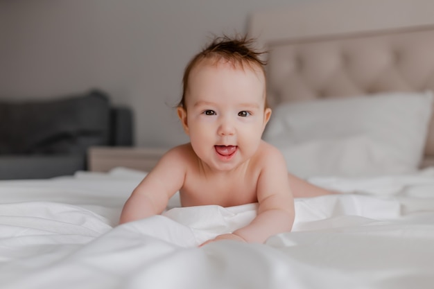 vrolijke baby ligt op zijn buik op een wit bed