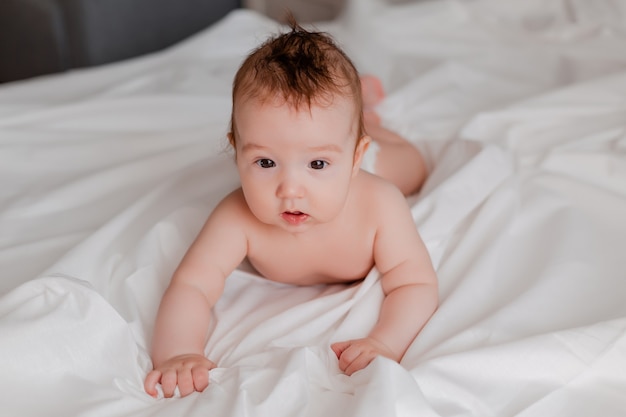 Vrolijke baby ligt op zijn buik op een wit bed