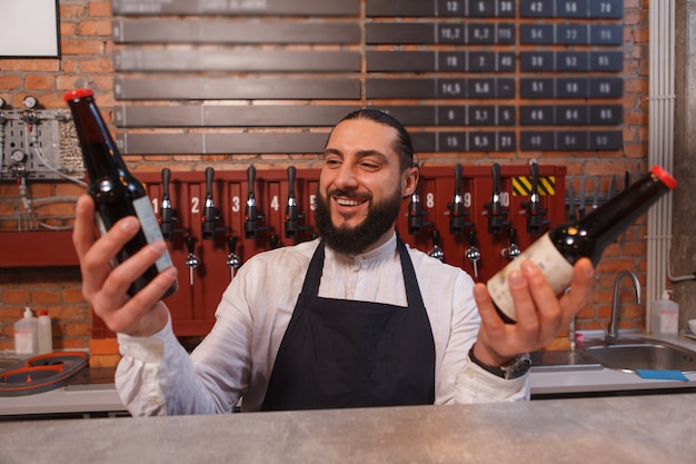 Vrolijke barman die tussen twee bierflesjes kiest die hij vasthoudt