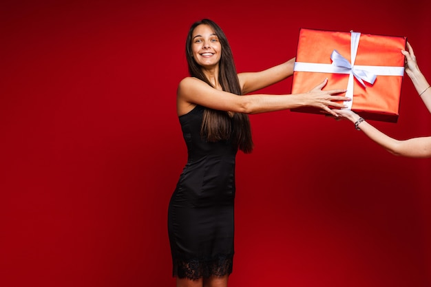 Vrolijke blanke vrouw met een aantrekkelijk uiterlijk met een grote doos met een cadeautje, foto geïsoleerd op rode muur