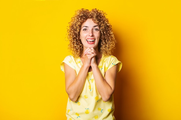 Vrolijke blije verrast curly-haired jonge vrouw op een gele achtergrond