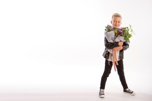 Vrolijke blonde modieuze jongen geeft boeket op witte studio