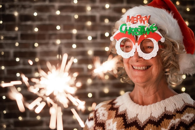 Vrolijke blonde senior vrouw met grappige bril en kerstmuts met sterretje licht oudere gelukkige dame vieren Kerstmis en nieuwjaar sprankelend in de nacht