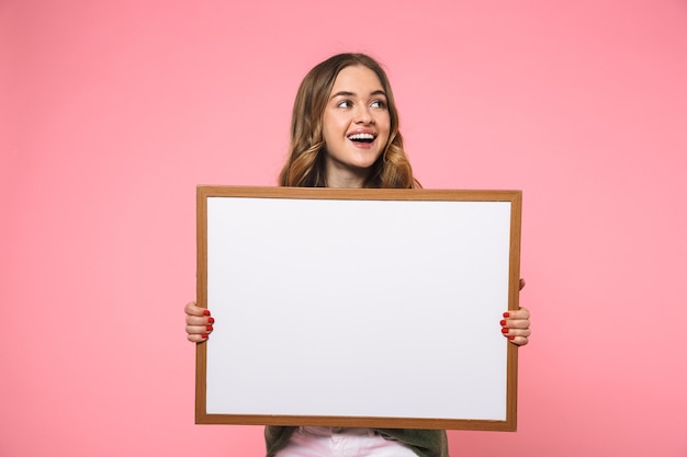 Vrolijke blonde vrouw die een leeg bord vasthoudt en wegkijkt over de roze muur