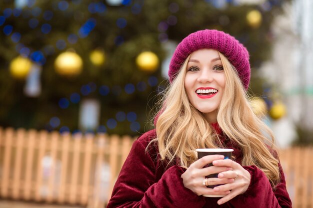 Vrolijke blonde vrouw die koffie drinkt in de buurt van de Cristmas-boom op het centrale plein in Kiev