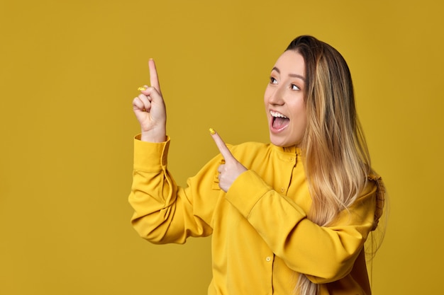 Vrolijke blonde vrouw die wegwijst op gele achtergrond