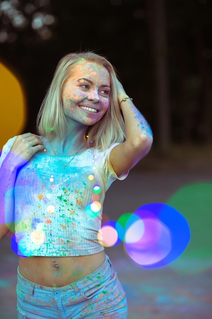 Vrolijke blonde vrouw met droog Holi-poeder op haar gezicht poserend met kleurrijke bloemenslinger