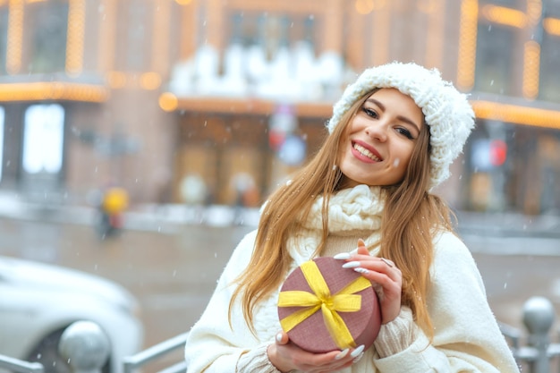 Vrolijke blonde vrouw met geschenkdoos met een strik op straat in de winter. Lege ruimte