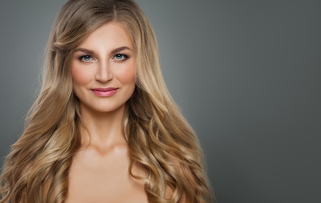 Vrolijke blonde vrouw met lang gezond krullend kapsel en heldere huid Haarverzorging en cosmetologie concept