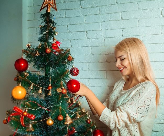 Vrolijke blonde vrouw siert kerstboom. Oudejaarsavond. Kerststemming.