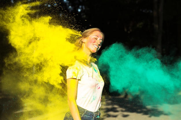 Vrolijke blonde vrouw speelt met gele en groene droge verf Holi in het park