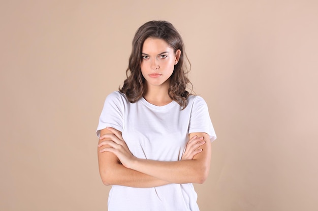 Vrolijke brunette vrouw gekleed in basiskleding kijken camera, geïsoleerd op beige background