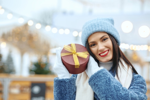 Vrolijke brunette vrouw in winterjas met een geschenkdoos op kerstmarkt. Ruimte voor tekst