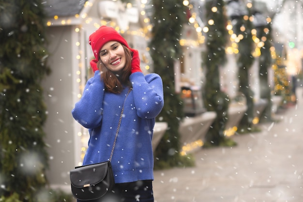 Vrolijke brunette vrouw wandelen op kerstmarkt tijdens de sneeuwval. Ruimte voor tekst