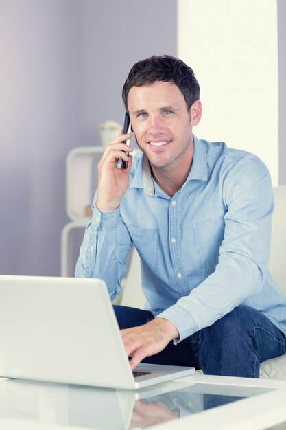 Vrolijke casual man met behulp van laptop en bellen