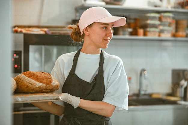 Vrolijke dame houdt dienblad met brood in de ambachtelijke bakkerijworkshop