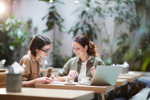 Vrolijke dames die kranten in koffie bekijken