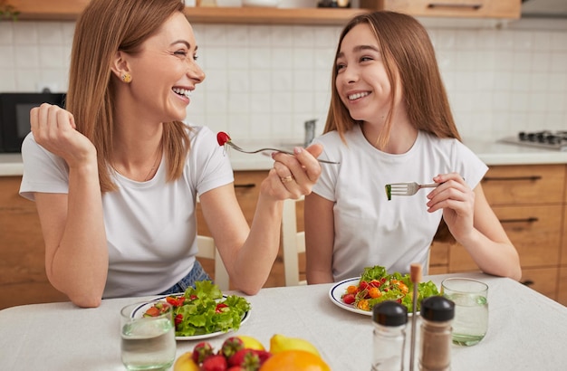 Vrolijke dochter en moeder die salade eten voor de lunch