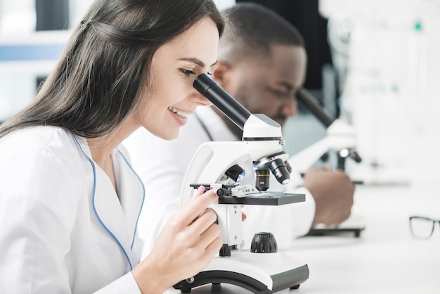 Foto vrolijke doktersvrouw die microscoop bekijkt