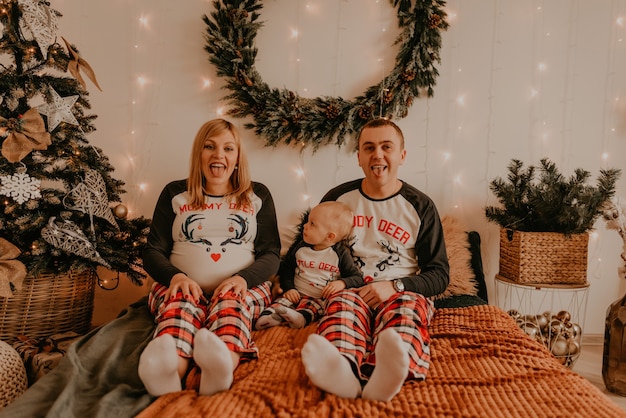 Vrolijke en gelukkige familie in pyjama's met kind zittend op bed in de slaapkamer. ouders tonen tongen. familiekleding voor het nieuwe jaar ziet eruit als outfits. Valentijnsdag Viering Geschenken