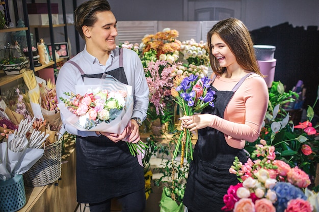 Vrolijke en gelukkige jonge man en vrouw staan en lachen. Ze houden boeketten bloemen. Mensen zitten in de kamer vol met planten.