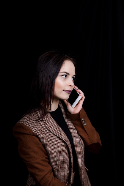 Vrolijke en succesvolle modeblogger voor jonge vrouwen praat emotioneel over de telefoon Mooie jonge vrouw in een casual grijs jasje houdt smartphone vast