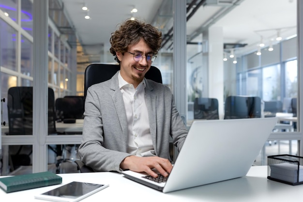 Vrolijke en succesvolle zakenman binnen kantoor werken met laptop bebaarde man glimlachend en typen