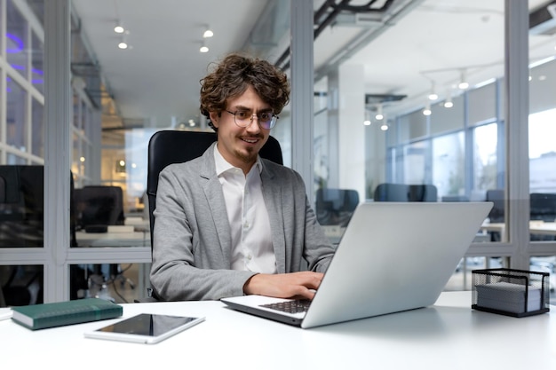 Vrolijke en succesvolle zakenman binnen kantoor werken met laptop bebaarde man glimlachend en typen