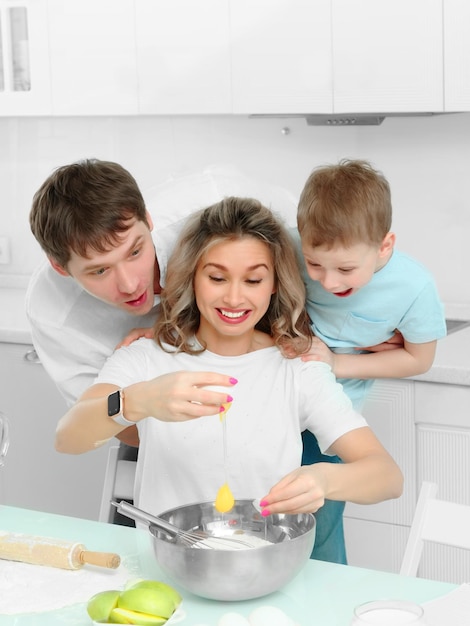 Vrolijke familie in keuken breekt ei in bord Ouders met jonge zoon bereiden samen heerlijk dessert