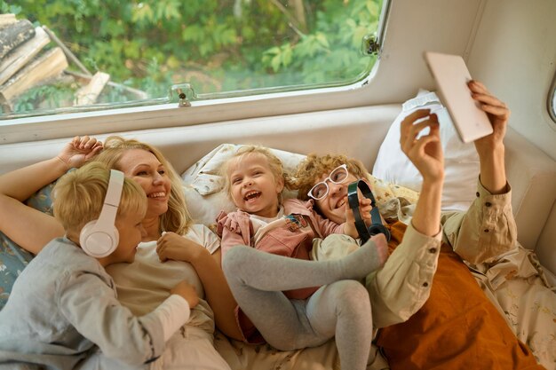 Vrolijke familie liggend in bed in camper, zomerkamperen. echtpaar met kinderen reizen in kamp auto, aanhangwagen interieur op achtergrond. campingavontuur, reizende levensstijl, vakantie met camper