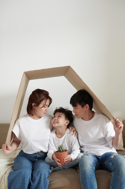 Vrolijke familie met bloempot zittend onder kartonnen dak thuis