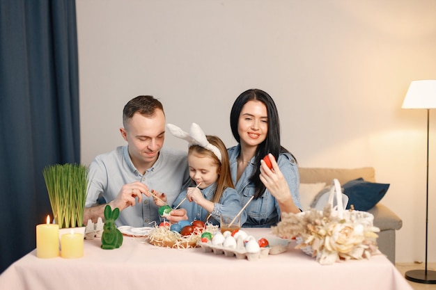 Vrolijke familiebijeenkomst aan tafel in moderne lichte keuken en samen paaseieren schilderen