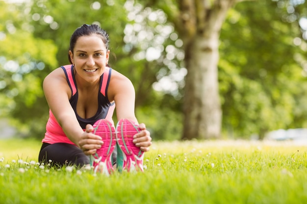 Vrolijke fit brunette die zich uitstrekt op het gras