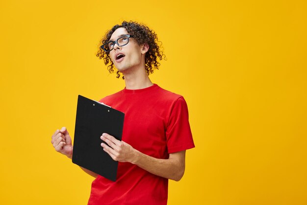 Vrolijke gelukkig bijziend jonge student man in rode tshirt grappige bril houdt tablet map met studie notities poseren geïsoleerd op over gele studio achtergrond vrije plaats voor advertentie onderwijs College concept