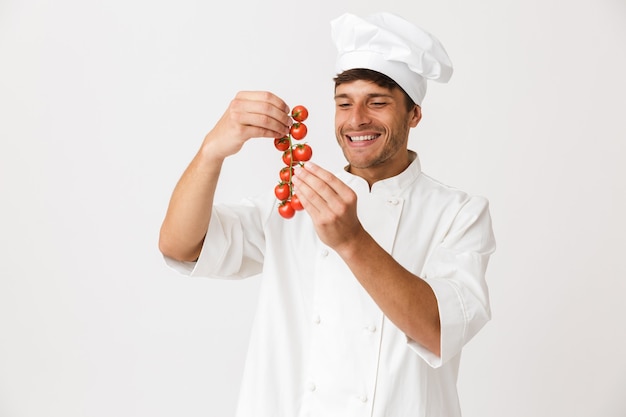 Vrolijke gelukkige jonge chef-kok geïsoleerd op wit bedrijf tomaten.