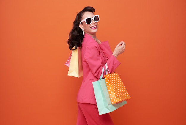 Foto vrolijke gelukkige vrouw die geniet van winkelen, ze draagt boodschappentassen op een oranje achtergrond