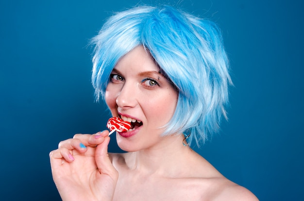 Vrolijke glamoureuze vrouw in blauwe pruik met een lolly in haar handen