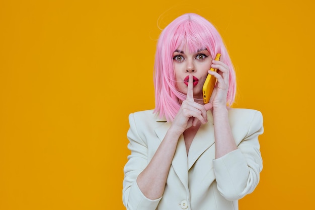 Vrolijke glamoureuze vrouw roze pruik praten aan de telefoon gele achtergrond